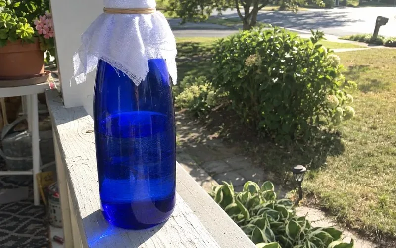 Blue glass bottle of water covered with muslin on a sunny porch rail