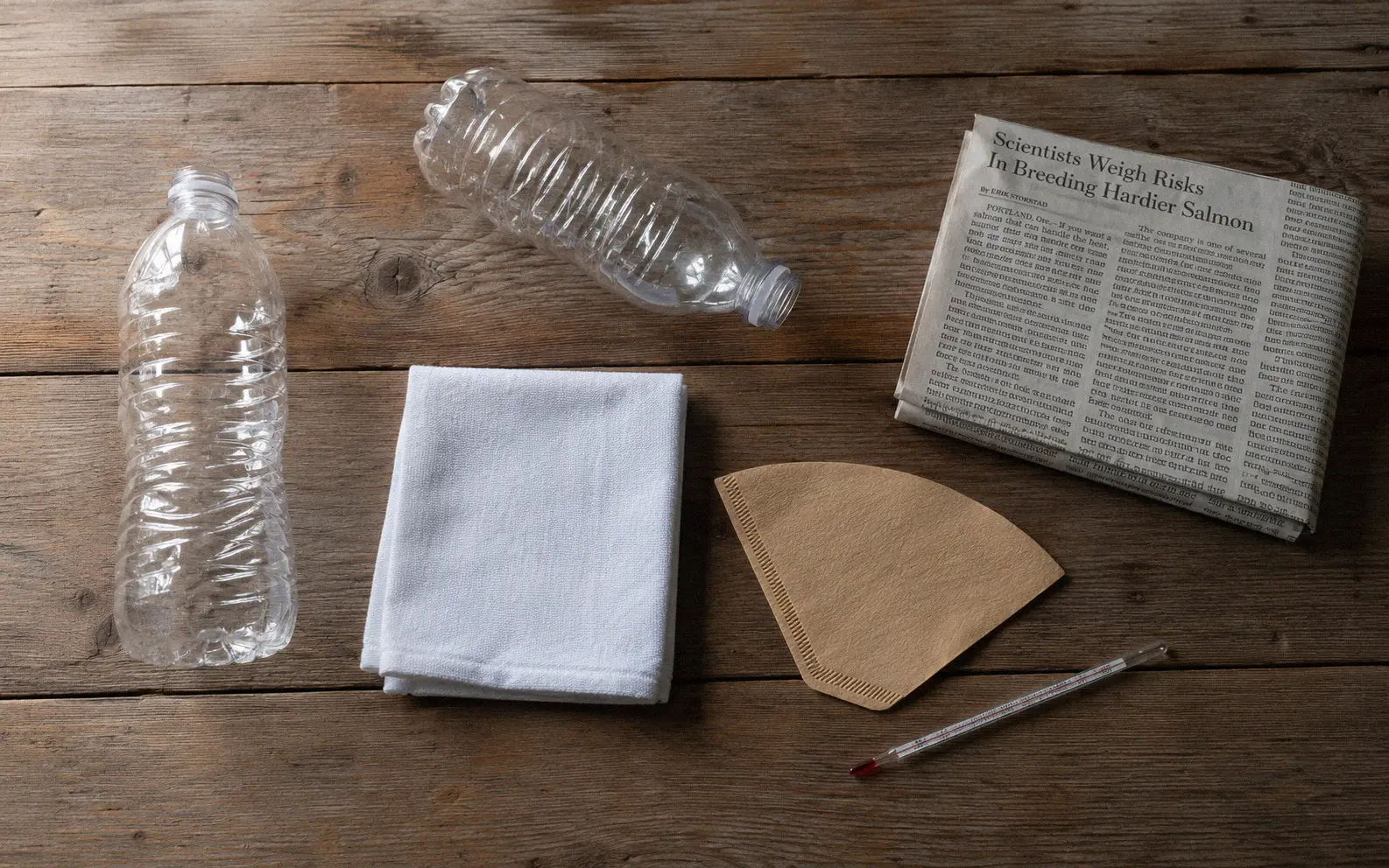 Materials needed for solarizing water including clear PET bottles, cloth filter, and newspaper